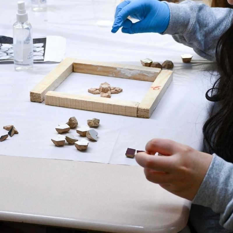 Hands placing zellige tiles onto a mosaic