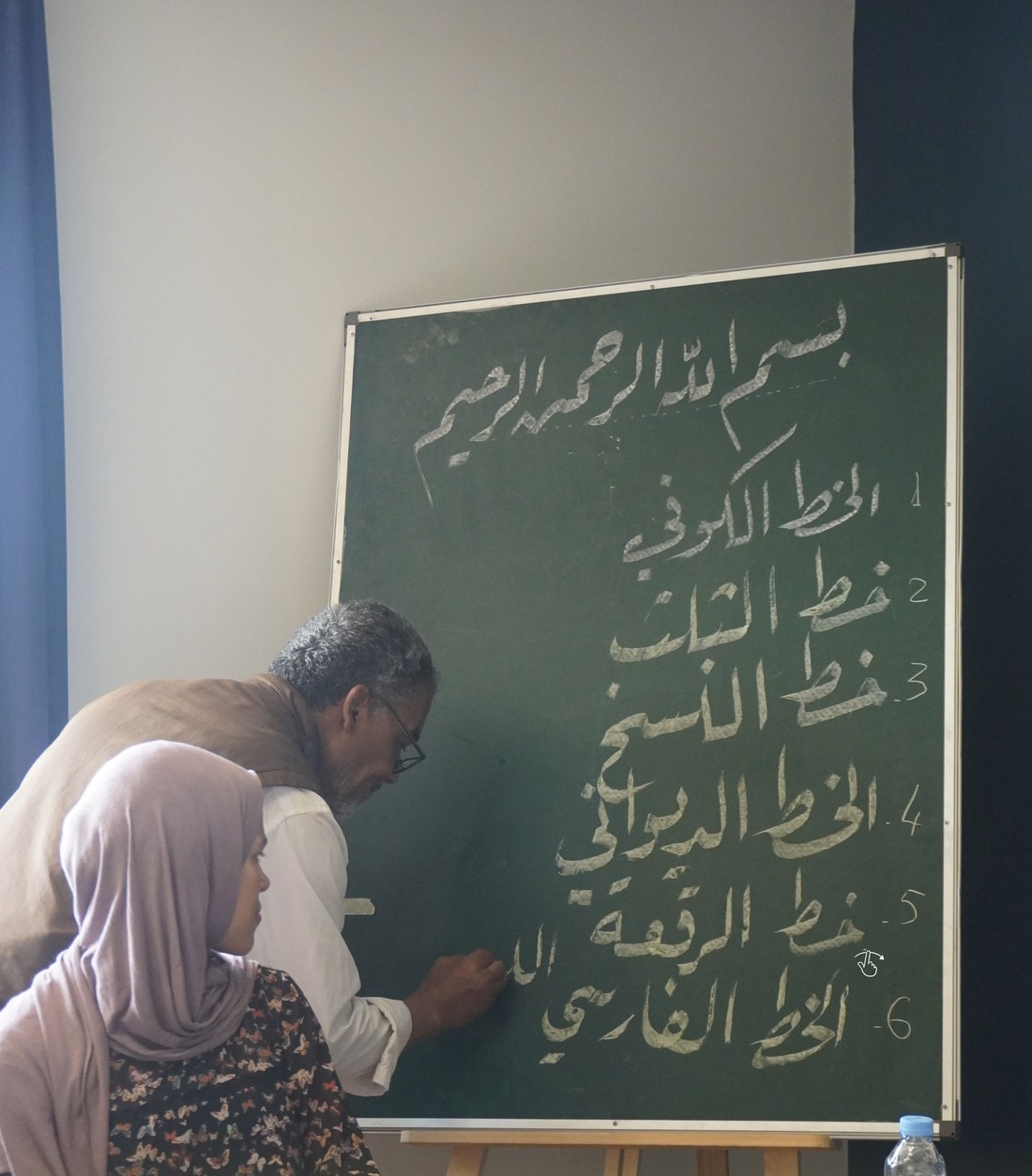 Instructor teaching Arabic calligraphy at a chalkboard